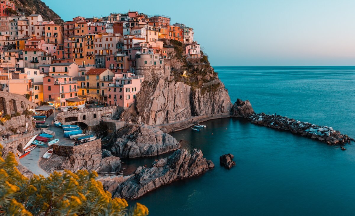 Mediterranean cliffside village with colorful stacked houses above a rocky harbor and small boats