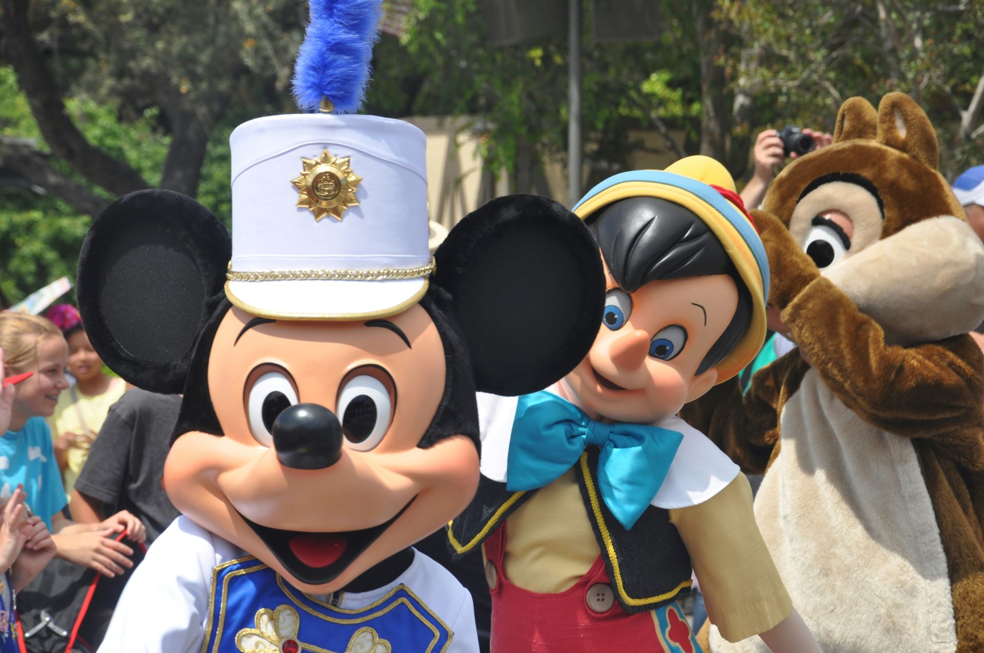 Mickey Mouse in white band hat with blue plume, Pinocchio and a chipmunk posing at parade