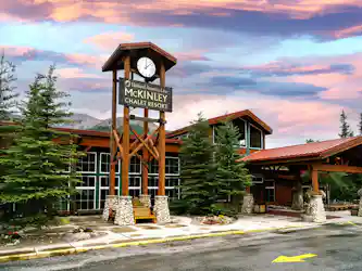 McKinley Chalet Resort wooden clock tower and entrance with evergreen trees at sunset.