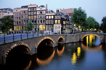 Evening Amsterdam canal with lit-arch bridge and row of tall narrow houses