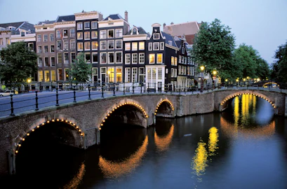 Evening Amsterdam canal with lit-arch bridge and row of tall narrow houses