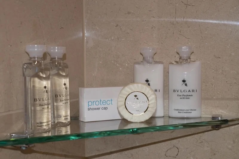 Glass shelf with Bvlgari toiletries: clear and white bottles, soap and shower-cap box.