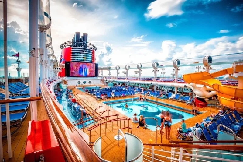 Cruise ship sun deck with central pool, yellow waterslide, lounge chairs and outdoor movie screen