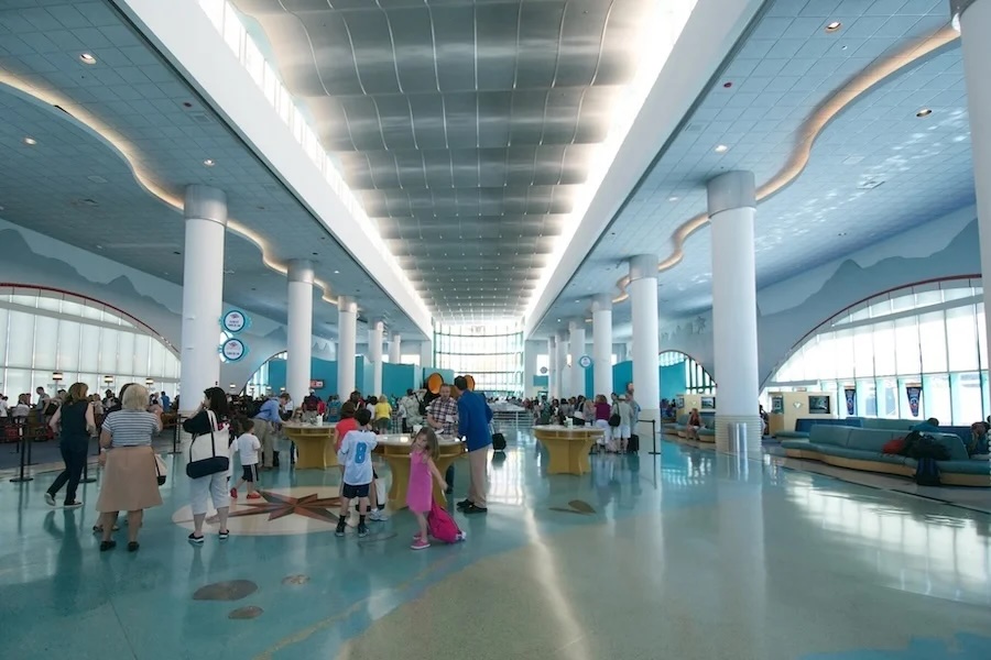 Busy blue travel terminal with high ceiling, white columns and families with luggage