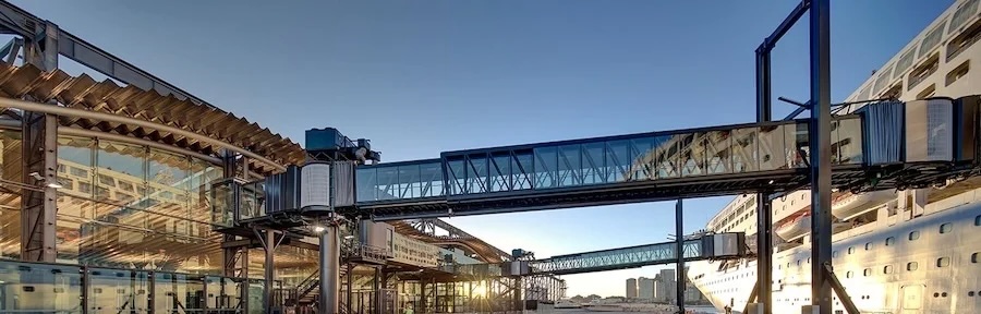 Glass enclosed boarding bridges connecting a terminal concourse to a docked cruise ship at sunset