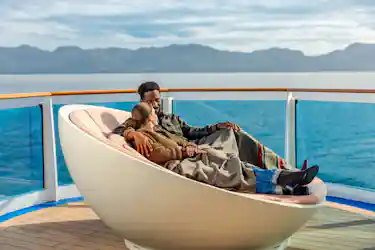 Couple cuddling under a blanket on a cruise ship deck lounger with ocean and mountains