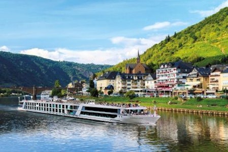 Tourist river cruise ship passing a riverside village with hillside vineyards and a church