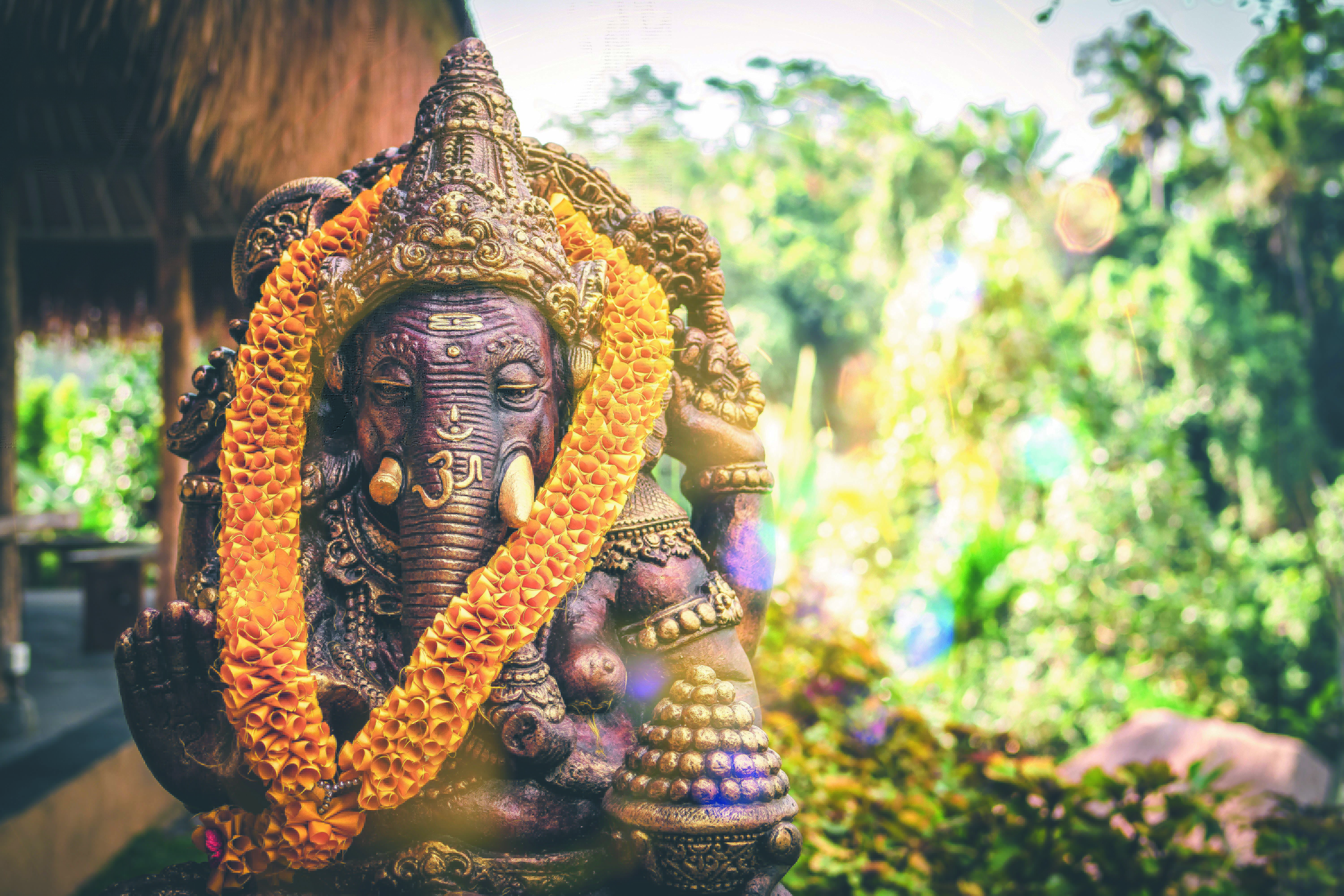 Bronze Ganesha statue wearing orange marigold garlands in a sunlit garden shrine