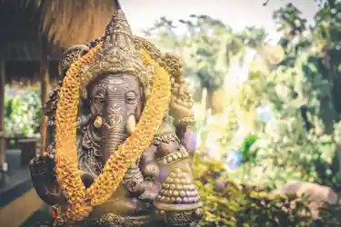 Bronze Ganesha statue wearing orange marigold garlands in a sunlit garden shrine