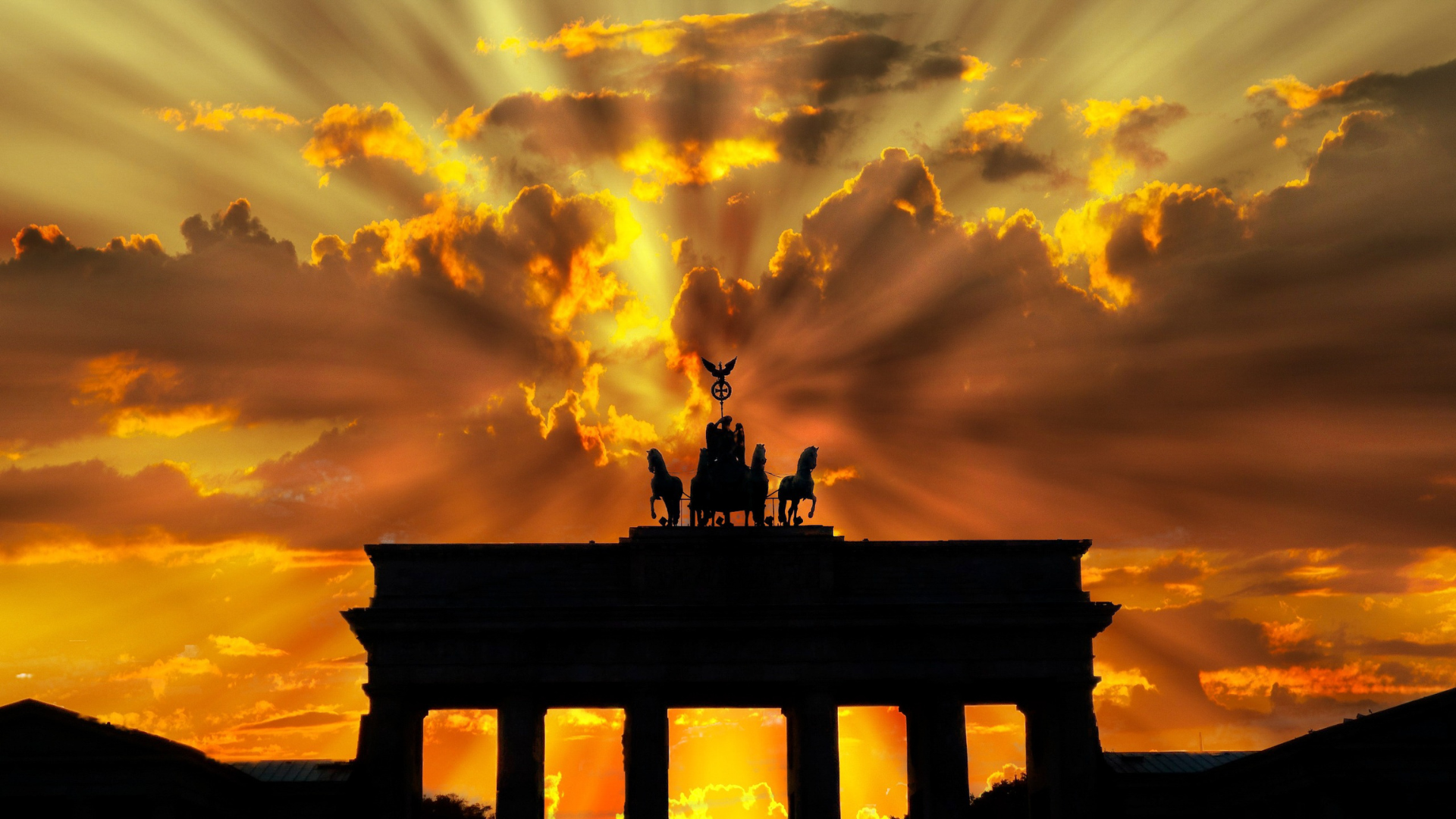 Four-horse chariot (Quadriga) atop Brandenburg Gate silhouetted against golden sunset rays