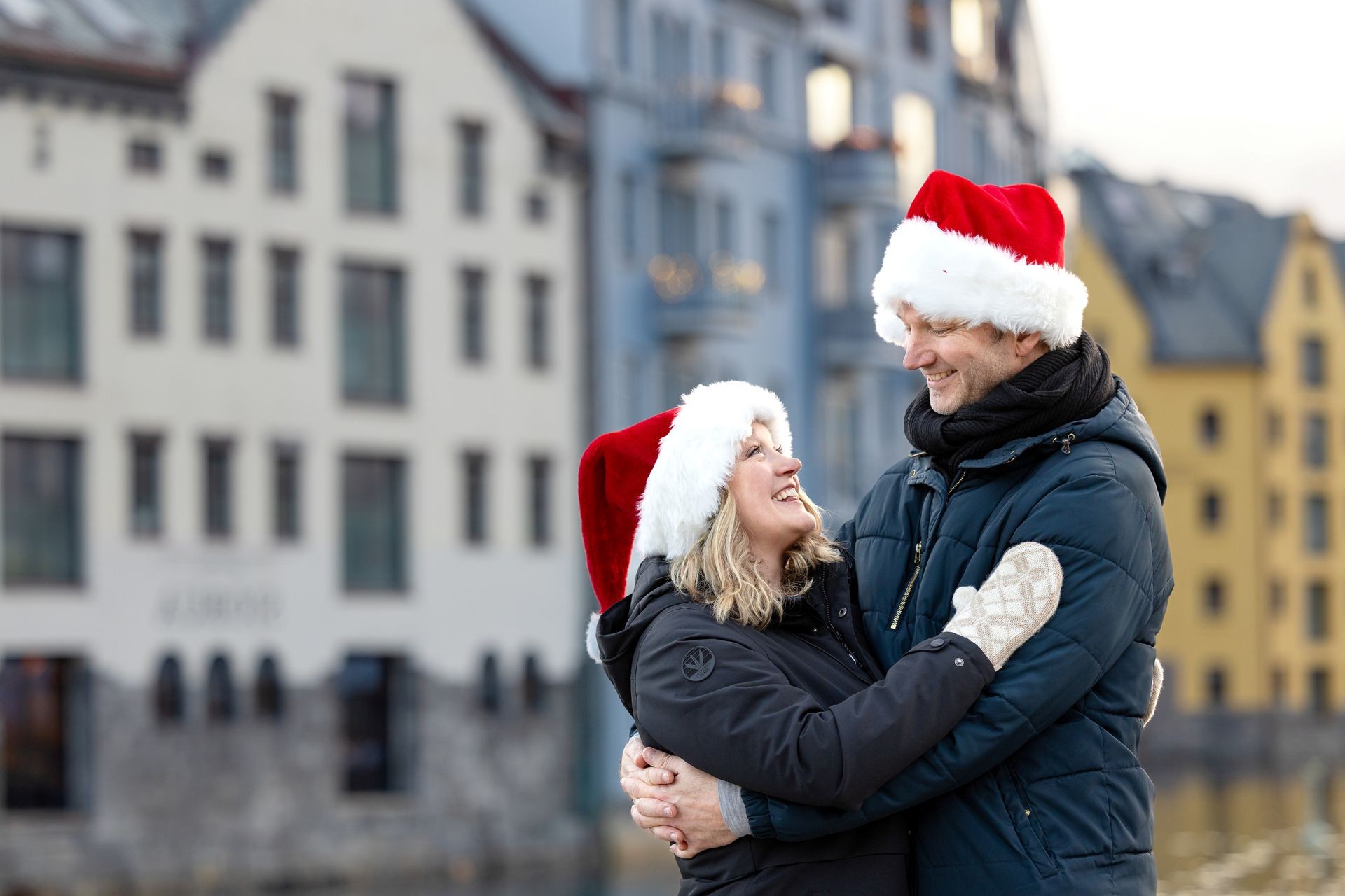 Smiling couple in winter coats and Santa hats embracing on a city waterfront