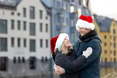 Smiling couple in winter coats and Santa hats embracing on a city waterfront