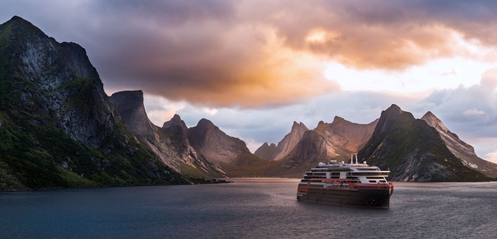 Cruise ship sailing in fjord surrounded by jagged mountains under orange sunset clouds