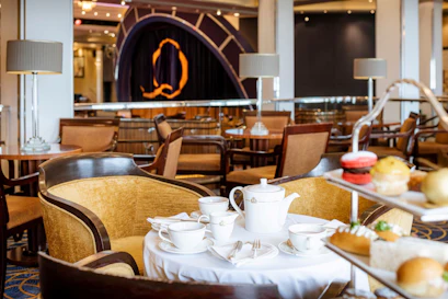 Afternoon tea set with white teapot, cups and pastries on table in elegant hotel lounge