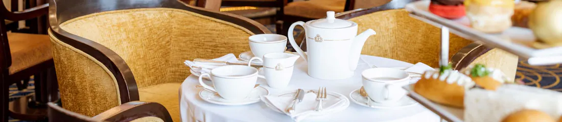 Afternoon tea set with white teapot, cups and pastries on table in elegant hotel lounge