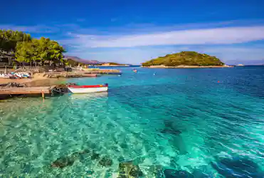Small red-and-white boat by a wooden pier, turquoise bay with a tree-lined shore and island.