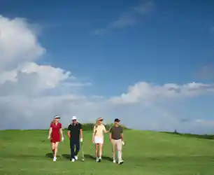 Four golfers walking across a green fairway under blue sky with clouds and a faint rainbow