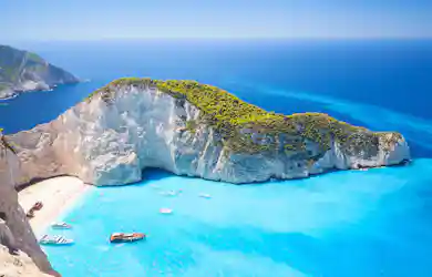 Limestone cliffs and green headland around turquoise bay with beach shipwreck and small boats.