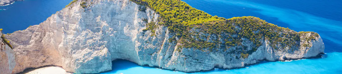 Limestone cliffs and green headland around turquoise bay with beach shipwreck and small boats.