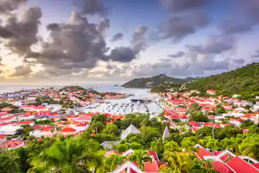 Marina-filled bay between green hills, red-roofed coastal town under cloudy sunrise sky