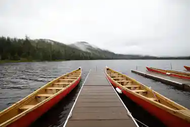 Wooden dock between red canoes on a calm lake with forested shore and distant mountains in mist