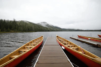 Wooden dock between red canoes on a calm lake with forested shore and distant mountains in mist