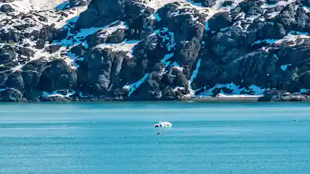 Turquoise glacial inlet with a small iceberg floating and snow-dusted rocky cliffs