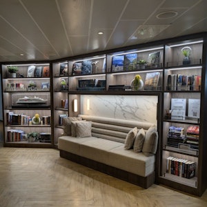 Illuminated built-in library nook with cushioned bench, pillows, bookshelves, model ship, plants