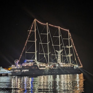Four-masted illuminated sailing yacht docked at night with lights reflected on water