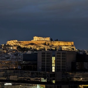 Illuminated Acropolis and Parthenon atop rocky hill above modern Athens at night