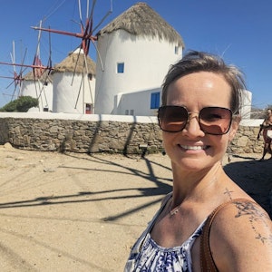 Smiling woman in sunglasses taking selfie by white thatched-roof windmills and stone wall