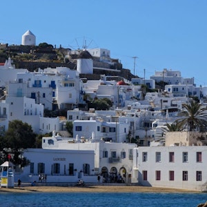 Whitewashed hillside houses with windmill above beachfront cafes and blue sea