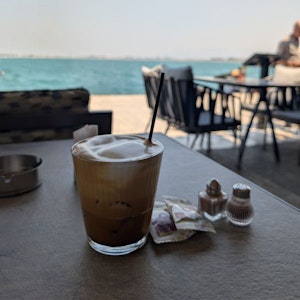 Iced coffee in glass with straw, sugar packets and salt shakers on café table by the sea