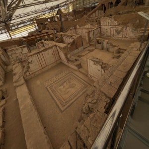 Excavated Roman house under canopy, exposed rooms with frescoes and central mosaic.