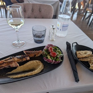 Restaurant table with grilled octopus, hummus, radicchio salad, pita, white wine and water bottle.