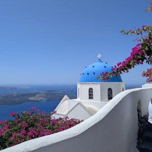 Blue-domed church and whitewashed terraces with pink bougainvillea overlooking Aegean Sea, Santorini