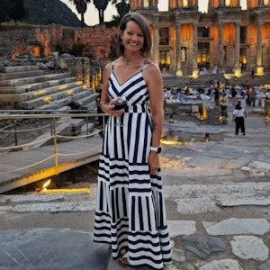 Woman in navy-and-white striped maxi dress holding a wine glass at illuminated ancient stone ruins
