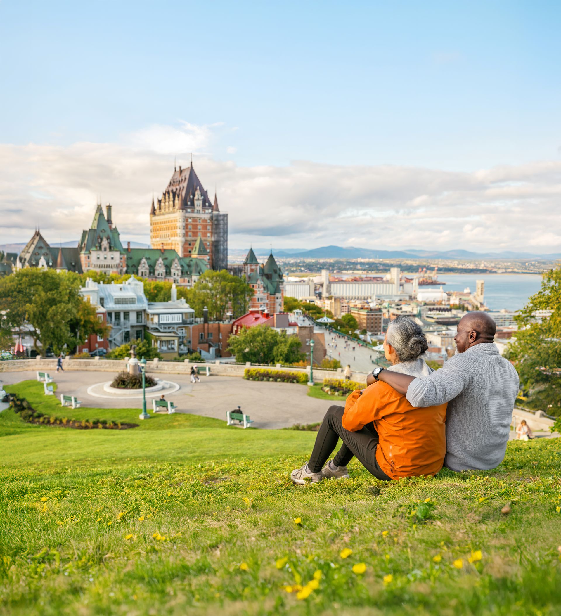 Older couple on a grassy hill, arm in arm, overlooking Château Frontenac and St. Lawrence River
