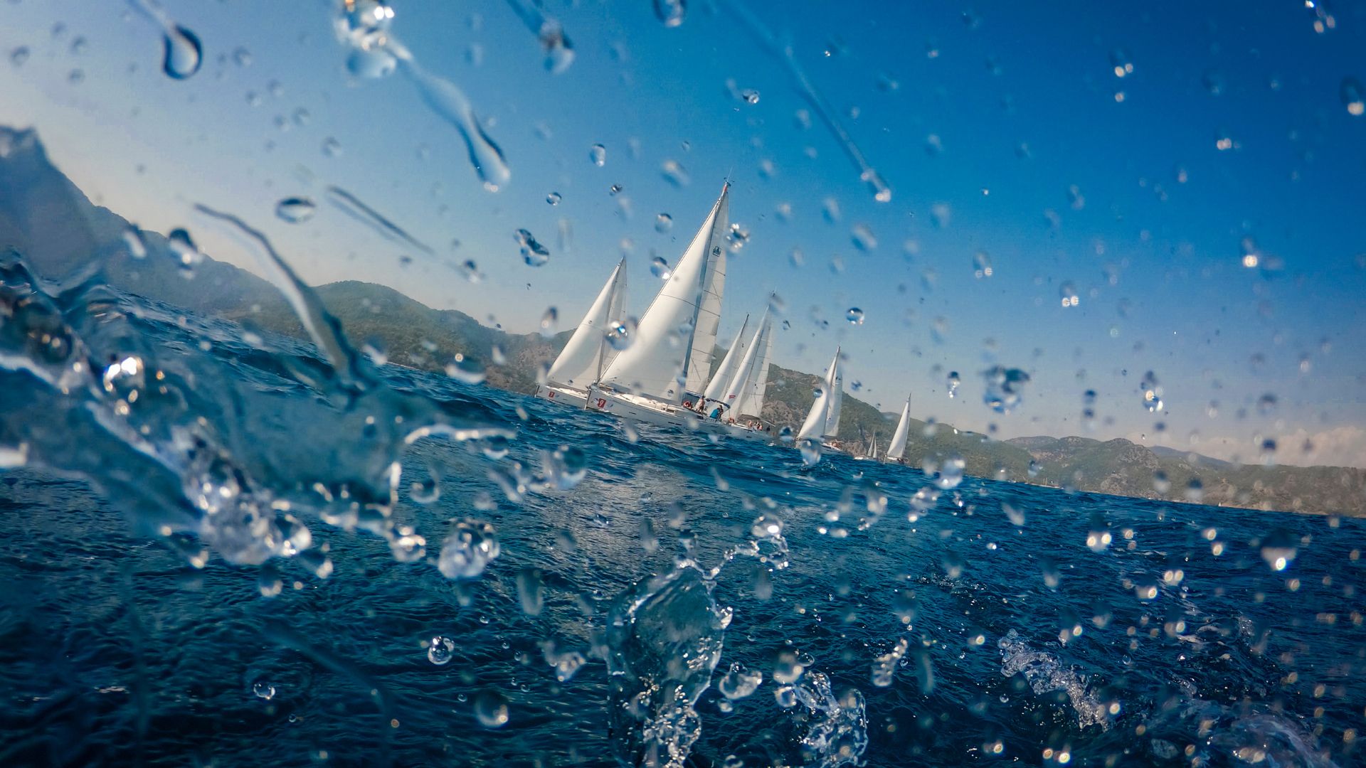 Water droplets on lens, sailboats racing on blue sea by green hills