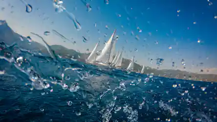 Water droplets on lens, sailboats racing on blue sea by green hills