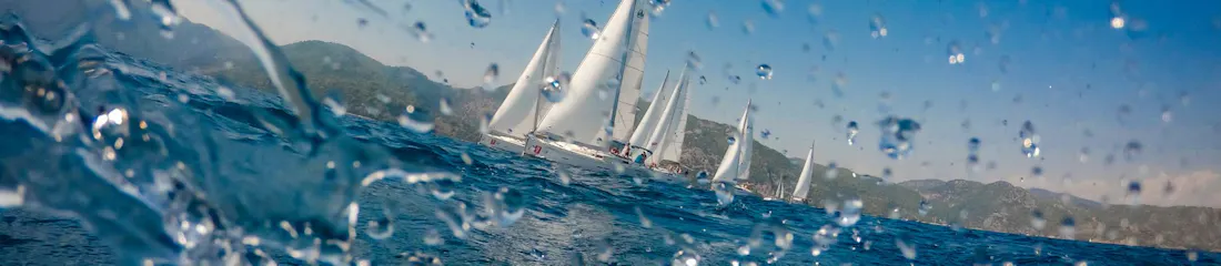 Water droplets on lens, sailboats racing on blue sea by green hills