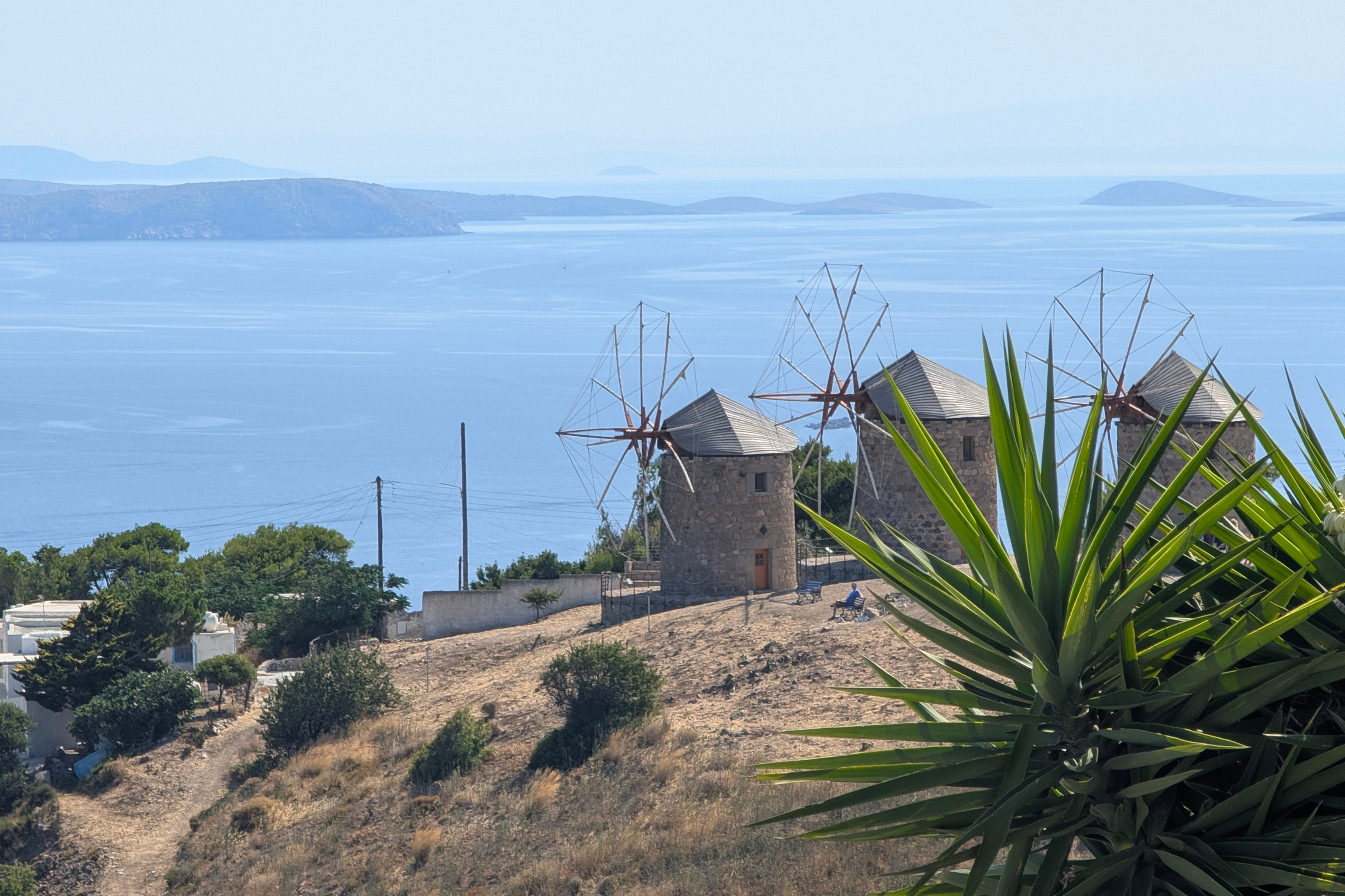 Three stone windmills above spiky agave, overlooking calm blue sea and distant islands