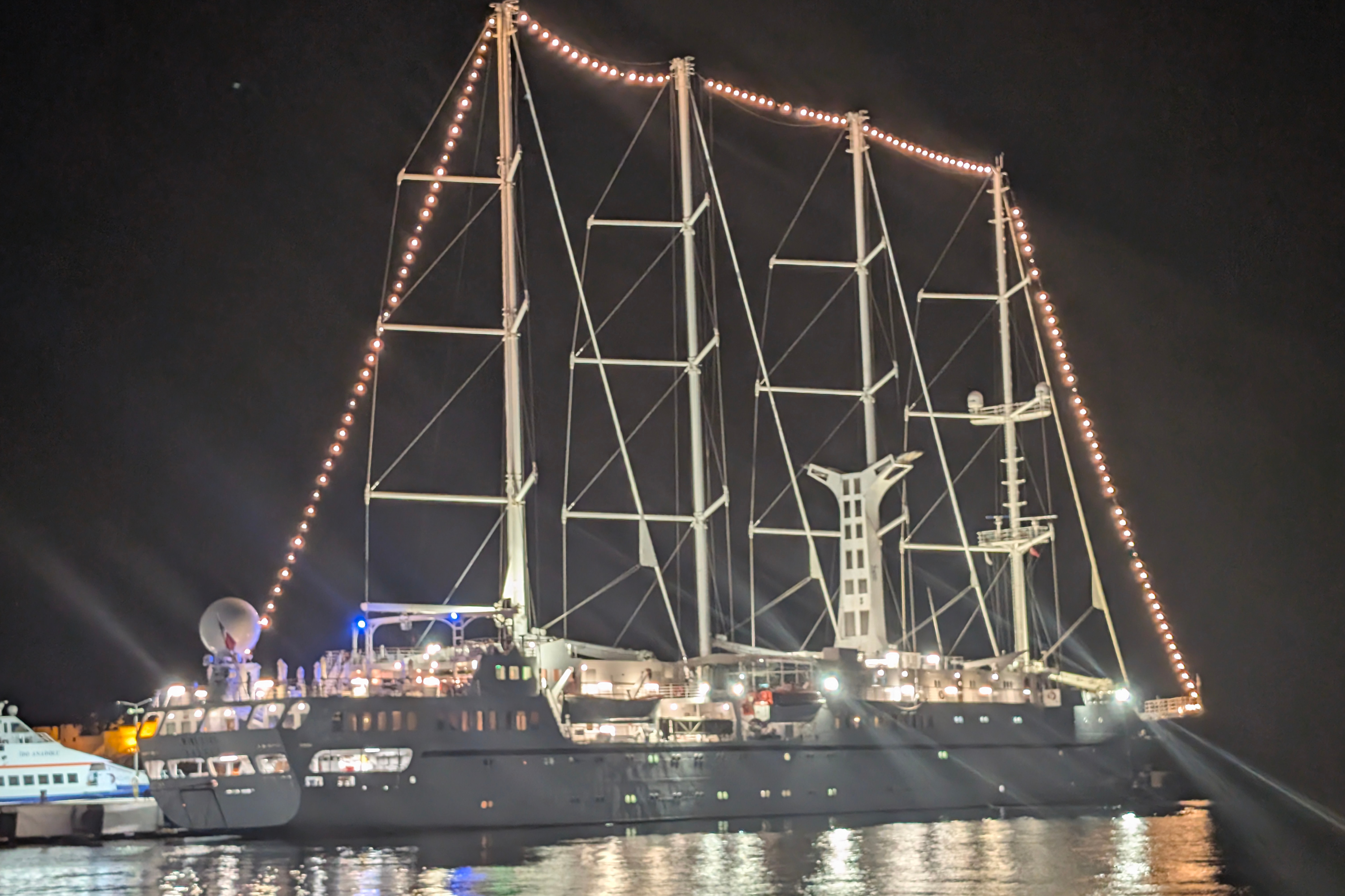 Large sailing yacht moored at night with illuminated masts and string lights reflected on water