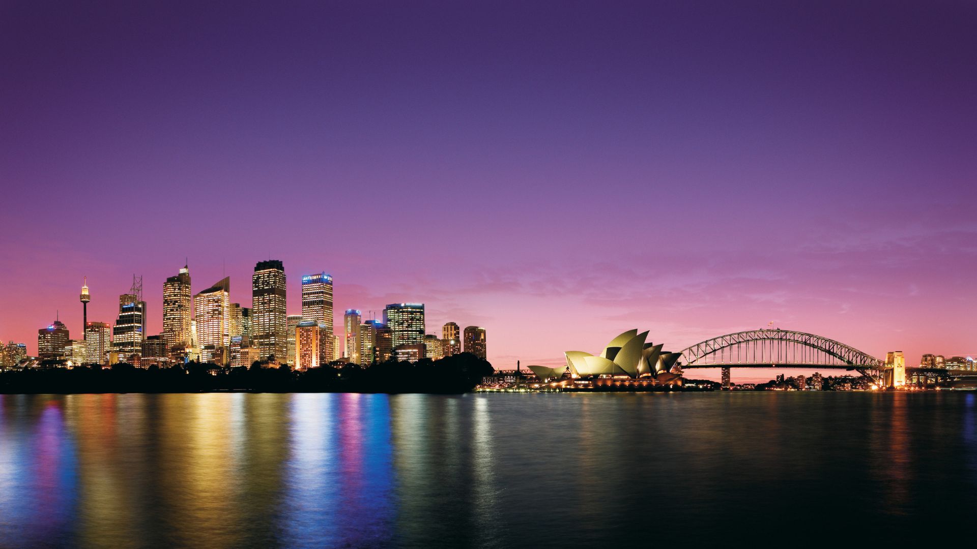 Sydney skyline at dusk: lit skyscrapers, Sydney Opera House and Harbour Bridge reflected in harbor