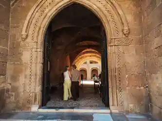 Couple walking arm-in-arm through carved stone arch into sunlit vaulted cloister