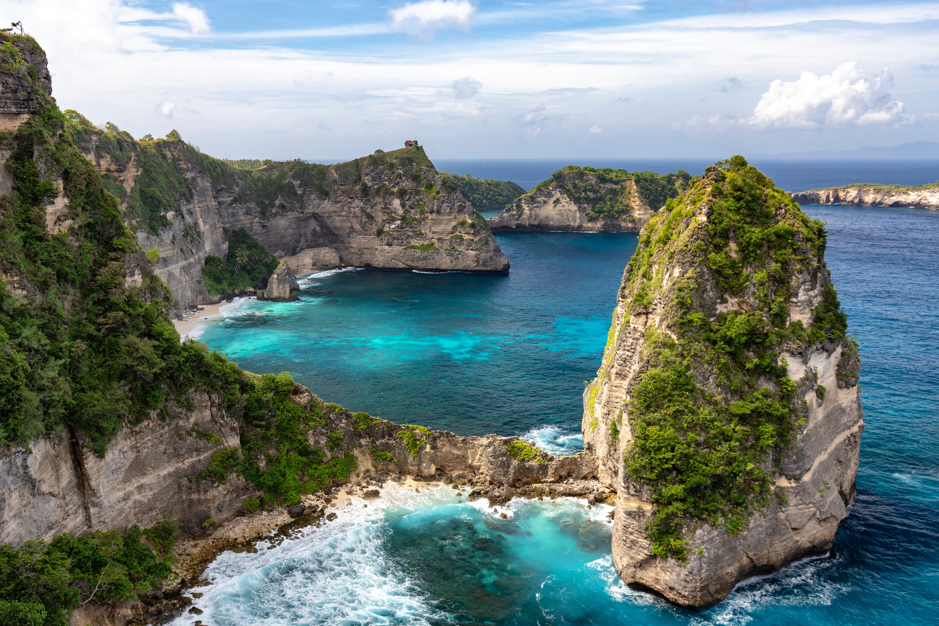 Turquoise bay framed by steep vegetated limestone cliffs and a tiny hilltop hut