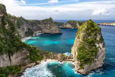 Turquoise bay framed by steep vegetated limestone cliffs and a tiny hilltop hut