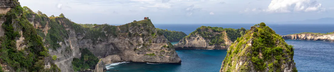 Turquoise bay framed by steep vegetated limestone cliffs and a tiny hilltop hut