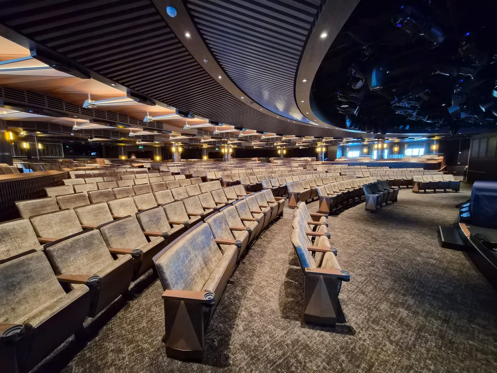 Empty curved auditorium with rows of upholstered seats, overhead lights and stage rigging