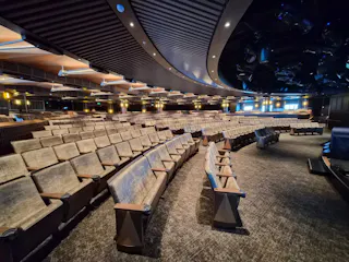 Empty curved auditorium with rows of upholstered seats, overhead lights and stage rigging